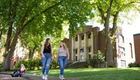 Two SPU students walk 和 talk in Tiffany Loop, with McKinley Hall in the background.
