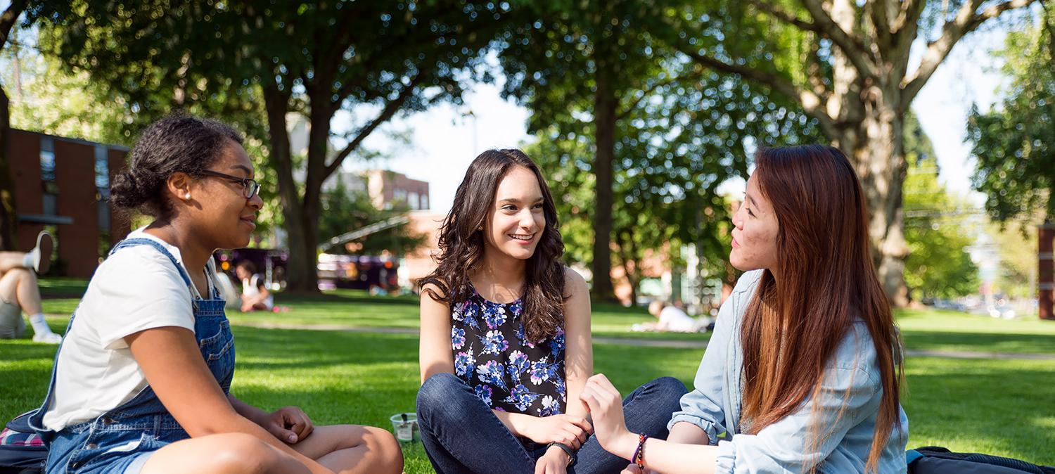 三个学生坐在蒂芙尼环路的草地上聊天